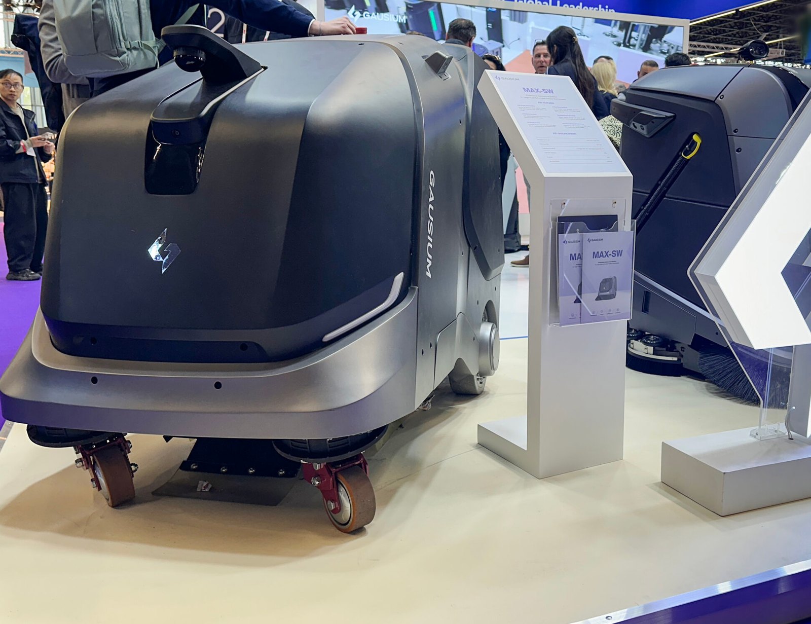 หุ่นยนต์กวาดพื้นกลางแจ้ง Gausium MAX-SW ตั้งแสดงข้างป้ายข้อมูล MAX-SW ที่งาน Interclean Amsterdam 2026
